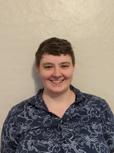 Katherine Wheeler wearing a shirt with an octopus print, in front of a plain off-white wall. She has short brown hair and is smiling.