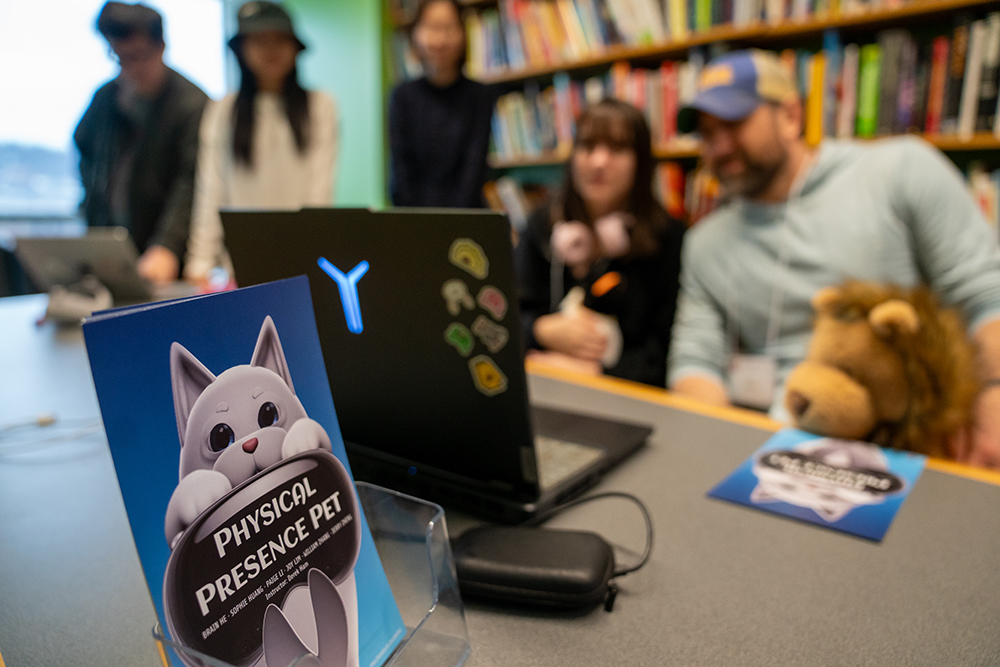 The Physical Presence Pet team tests their game with the poster in the foreground